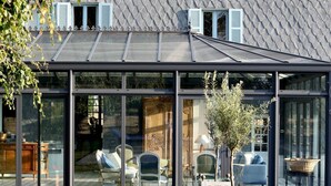 A modern house with a glass conservatory, outdoor seating, and a swimming pool.