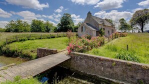 A stone house with a wooden bridge over a water channel, surrounded by greenery and trees. - Chateau Les Douves - Eight Bedroom Castle, Sleeps 14 (Fontenay-sur-Mer)