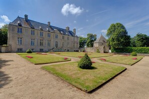 A large, historic stone building with a symmetrical facade, a central tower, and a well-maintained garden with geometric flower beds and hedges. - Chateau Les Douves - Eight Bedroom Castle, Sleeps 14 (Fontenay-sur-Mer)