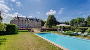 A swimming pool with lounge chairs, a stone building in the background, and well-maintained gardens. - Chateau Les Douves - Eight Bedroom Castle, Sleeps 14 (Fontenay-sur-Mer)