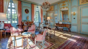 A room with a piano, a chandelier, and a large window with curtains. - Chateau Les Douves - Eight Bedroom Castle, Sleeps 14 (Fontenay-sur-Mer)