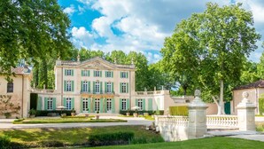 A large, classical building with a symmetrical facade, a central entrance, and a formal garden with a fountain.