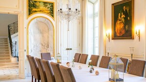 A formal dining room with a long table, chairs, chandeliers, and classical paintings.