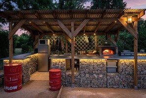 Una cocina exterior con pared de piedra, una parrilla y una pérgola de madera.
