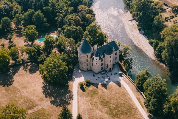A castle-like building with a moat, surrounded by trees and a river.