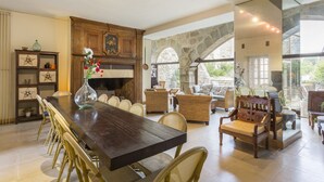 A spacious dining area with a long wooden table, wicker chairs, and a stone archway leading to an outdoor patio.