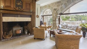 A cozy living area with wicker furniture, a stone fireplace, and a view through an arched stone structure.