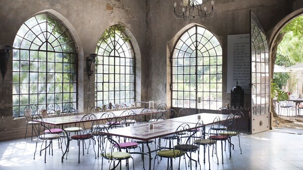 Ein großer Raum mit langem Tisch und Stühlen, Rundbogenfenstern und einem Chandelier.