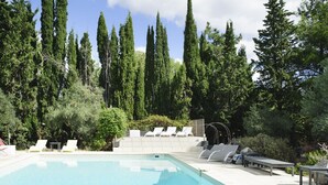 Ein Pool mit Liegestühlen und einer Pergola, umgeben von hohen Bäumen.