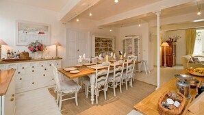 Un coin repas avec une table en bois dressée pour six personnes, entourée de chaises blanches. On aperçoit, au fond, un buffet blanc aux portes vitrées.