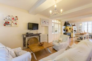 Una sala de estar con chimenea, muebles blancos, un televisor y obras de arte en las paredes.