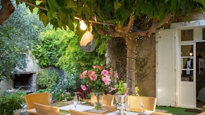 Un espace extérieur aménagé pour les repas, avec des chaises et des tables en osier, un mur en pierre et un luminaire suspendu.