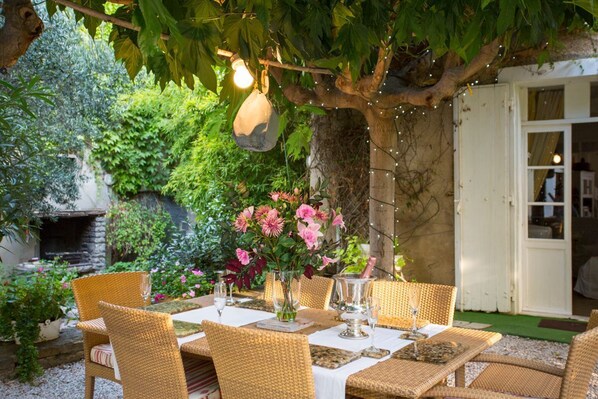 Un espacio exterior para comer con sillas y mesas de mimbre, un muro de piedra y una lámpara colgante.