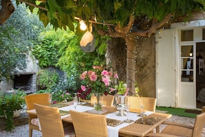 An outdoor dining area with wicker chairs and tables, a stone wall, and a hanging light fixture.