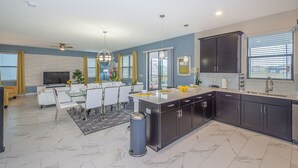 A modern kitchen with dark cabinets, a central island, and a dining area with a TV and seating. - Luxury Villa Storey Lake, 15min→Disney, private pool + hot tub + No Extra Fees (Kissimmee)