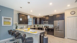 A modern kitchen with dark cabinets, stainless steel appliances, a central island with bar stools, and a clock on the wall. - Luxury Villa Storey Lake, 15min→Disney, private pool + hot tub + No Extra Fees (Kissimmee)