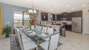 A modern kitchen with dark cabinets, stainless steel appliances, and a dining area with a glass table and white chairs. - Luxury Villa Storey Lake, 15min→Disney, private pool + hot tub + No Extra Fees (Kissimmee)
