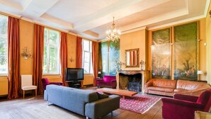 Un salon avec une cheminée, un téléviseur et un lustre.