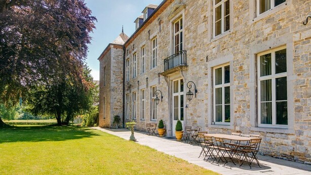 A stone building with a paved patio, outdoor seating, and a tree.