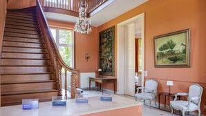 Un grand escalier menant à un palier agrémenté d’un lustre, d’un grand tableau floral et d’un comptoir d’accueil avec des chaises.