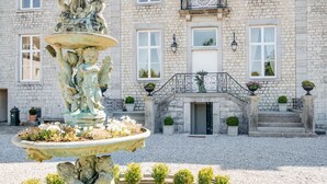 A stone building with a fountain, steps, and potted plants.