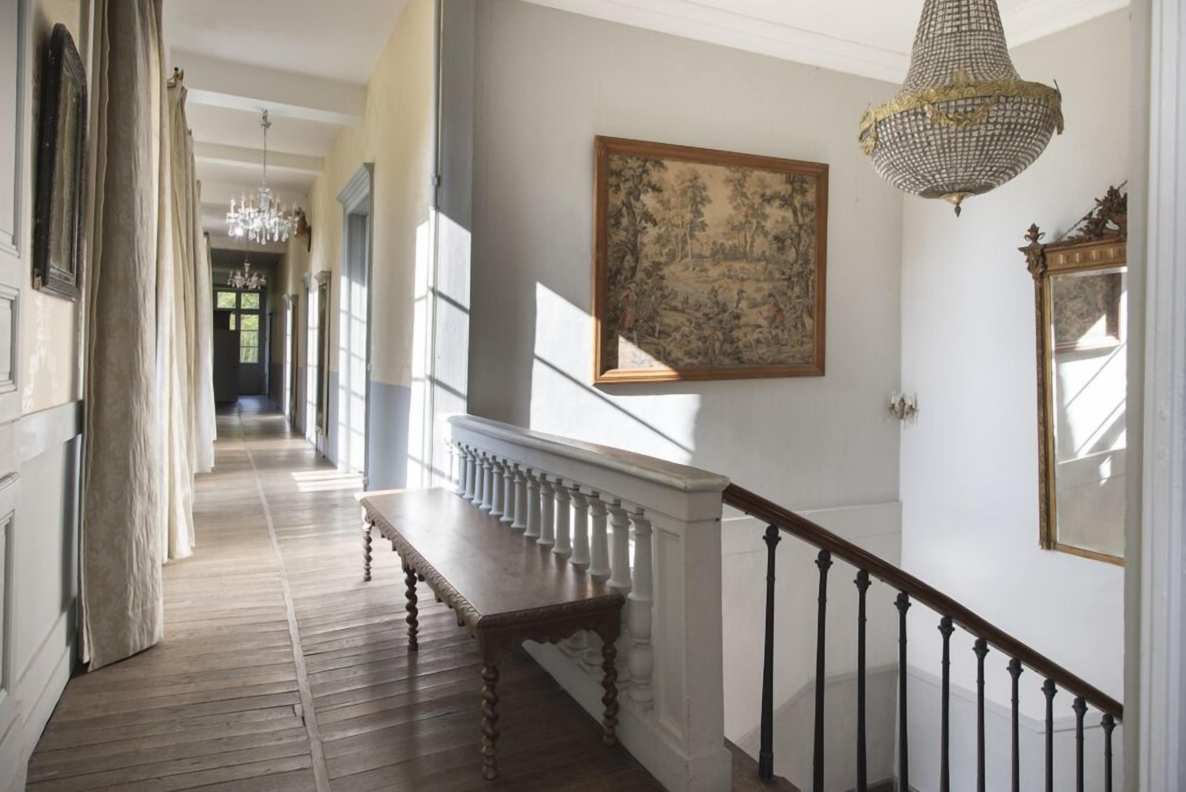 Een hal met een houten bank, een kroonluchter en een schilderij aan de muur.