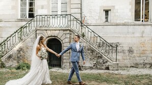A couple holding hands in front of a stone building with a staircase.