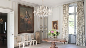 A formal dining room with a large painting, a chandelier, and a table with flowers.