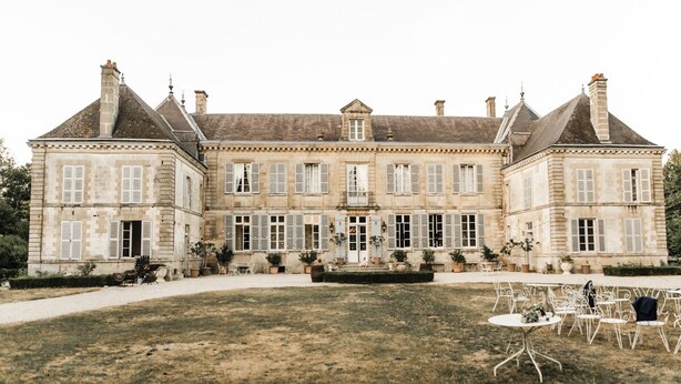 A large, historic stone building with symmetrical architecture, featuring multiple chimneys and a central entrance.