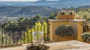 Un balcón con vista a un paisaje montañoso, un recipiente de vidrio con una planta y una maceta en la pared.