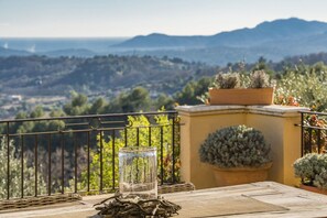 A balcony with a view of a mountainous landscape, a glass container with a plant, and a potted plant on the wall.