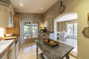 A kitchen with a dining area, a fruit basket on the table, and a clock on the wall.