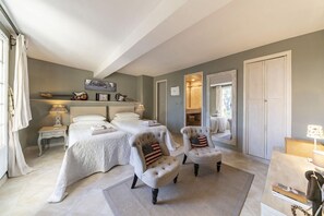 Ein Schlafzimmer mit zwei Betten, einem Sessel, einem Kleiderschrank und einem Spiegel.