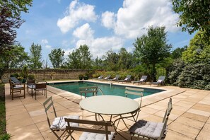 A pool area with lounge chairs, a table, and a stone wall.