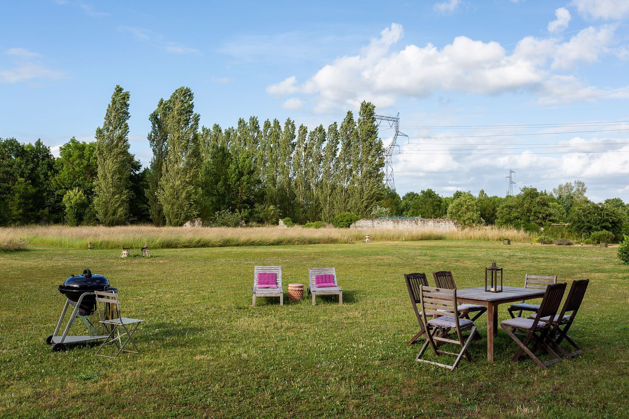 Een terras buiten met een tafel, stoelen, een barbecue en een picknicktafel met kussens.
