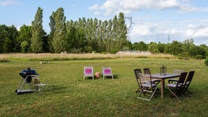 Ein Sitzbereich im Freien mit Tisch und Stühlen, einem Grill und einem Picknicktisch mit Kissen.