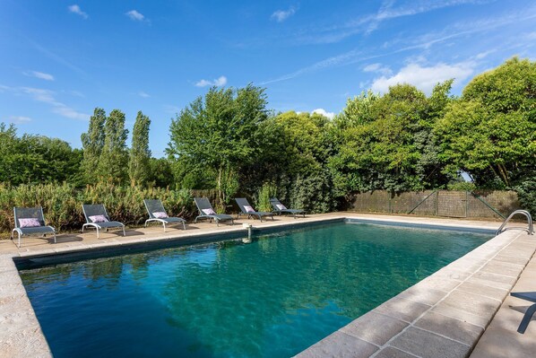 A swimming pool with lounge chairs and a stone border.