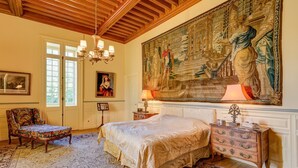 Une chambre spacieuse avec un grand lit, un plafond en bois décoré, une grande tapisserie et des meubles classiques.