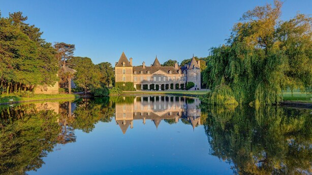 Un grand bâtiment historique à la façade symétrique, doté d’une tour centrale et d’un bassin d’eau dont la surface reflète l’environnement, situé à l’avant.