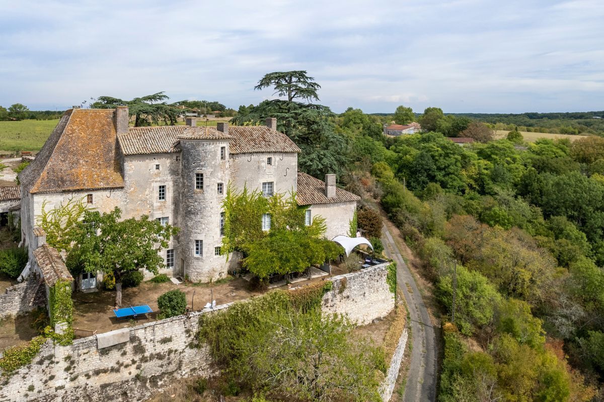 Un bâtiment en pierre doté d’une cour intérieure, entouré d’arbres et d’un mur de pierre.