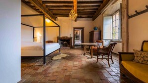 Een landelijke kamer met een hemelbed, een open haard, een eettafel met stoelen en een bank.