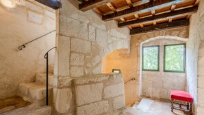 A stone-walled room with a wooden staircase, a bench, and a window with a view of greenery.