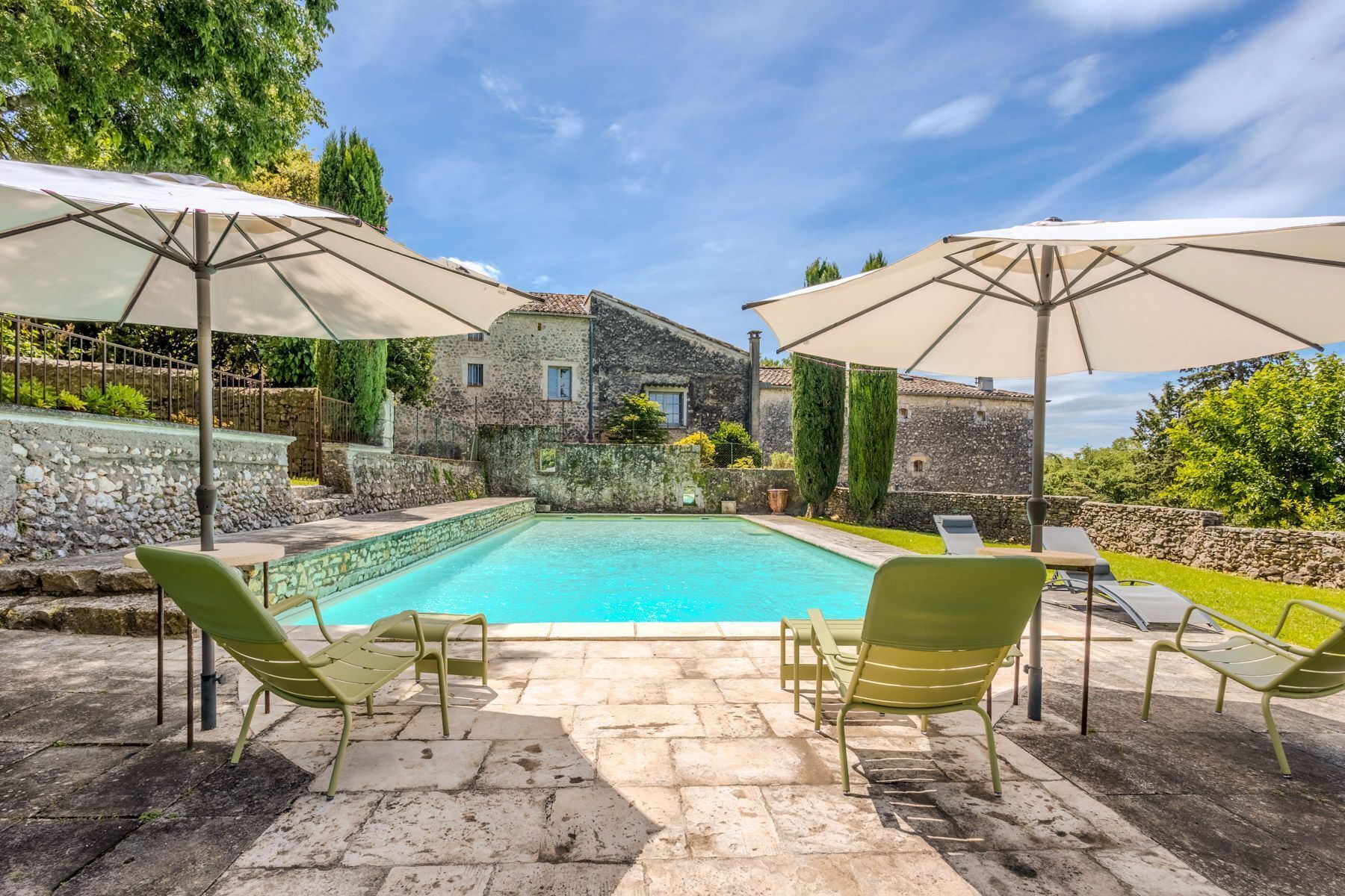 Une piscine entourée de murs de pierre et de verdure, avec des chaises longues et des parasols.