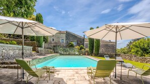 A swimming pool with lounge chairs and umbrellas, surrounded by stone walls and greenery.