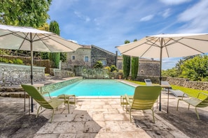 A swimming pool with lounge chairs and umbrellas, surrounded by stone walls and greenery.