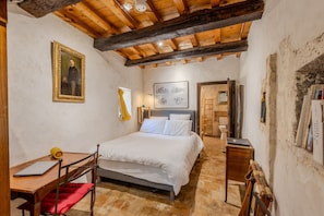 A bedroom with a bed, a desk, a chair, a wooden ladder, and a painting on the wall.