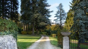 Un camino de grava que serpentea por un jardín con árboles frondosos y una jardinera de piedra.