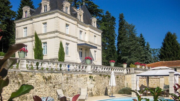 Un edificio grande con piscina, paredes de piedra y plantas en macetas.