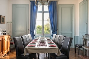 A dining room with a long table set for six, flanked by blue curtains and a chandelier. - Chateau Du Mas - Five Bedroom Castle, Sleeps 10 (Dignac)