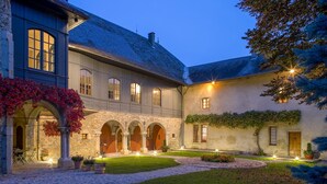 Une cour avec un bâtiment en pierre, des arcades et des plantes en pot.
